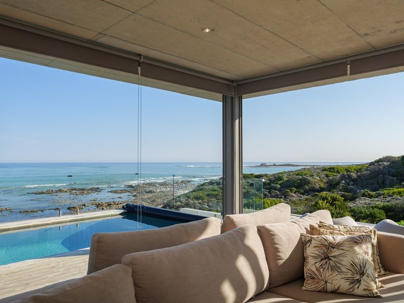 A modern covered patio featuring timber decking and a glass balustrade, overlooking a private swimming pool with expansive ocean views.