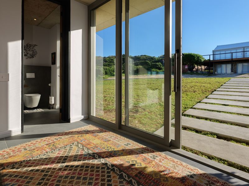 Modern living space featuring polished concrete floors, slatted timber accents, and large sliding glass doors opening onto a landscaped garden with a concrete pathway.