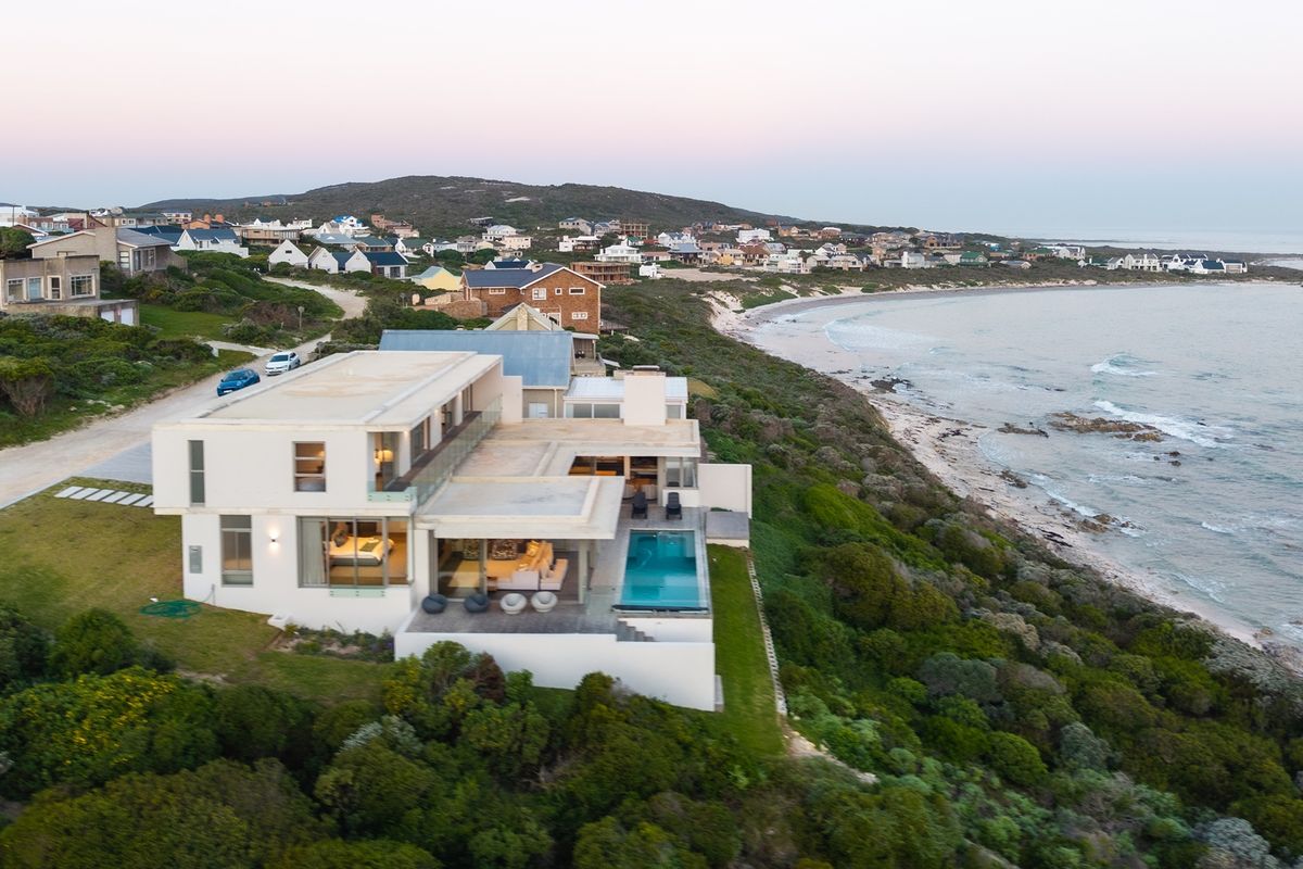 Aerial view of a modern coastal residence featuring a swimming pool, expansive terraces, and direct proximity to the ocean.