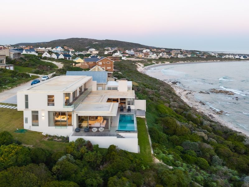 Aerial view of a modern coastal residence featuring a swimming pool, expansive terraces, and direct proximity to the ocean.