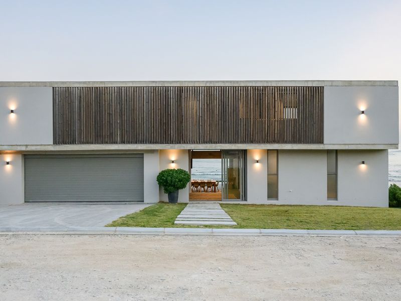 Modern coastal residence featuring a concrete facade, timber slat detailing, integrated garage, and a paved entrance path with ocean views.