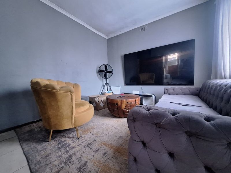A living room space featuring neutral grey walls, coving, and a ventilation grille, providing a functional area for relaxation.