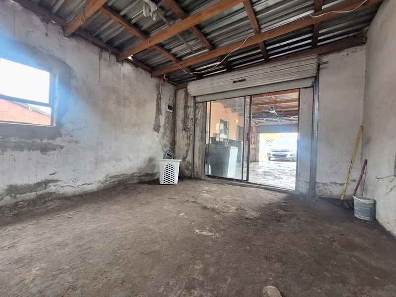 An unfinished garage space featuring exposed timber roof trusses, concrete flooring, and a sliding glass door leading to the exterior.