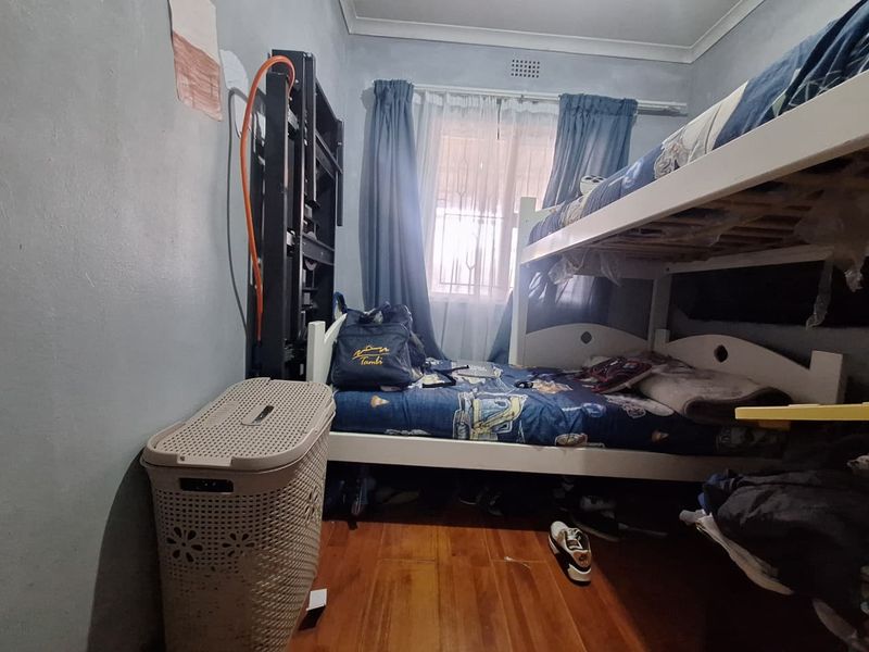 A compact bedroom featuring timber flooring and security bars on the window, currently utilized as a children's room.