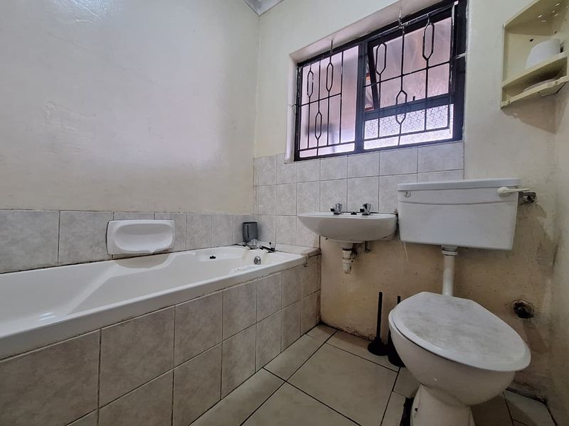 A dated bathroom featuring a bathtub, wall-mounted basin, and toilet, requiring cosmetic updates and refurbishment to improve its overall condition and appeal.