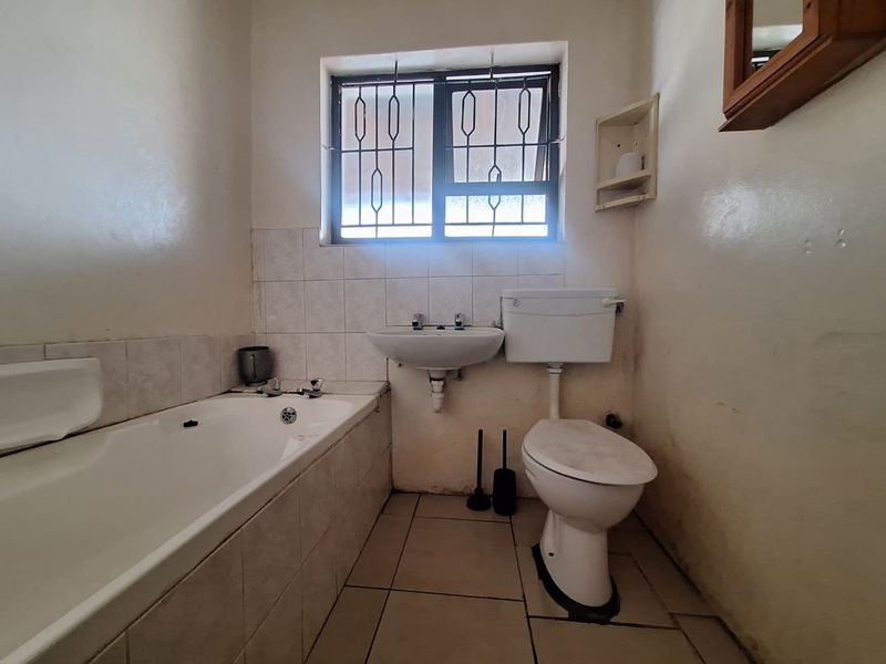 A functional bathroom featuring a standard bathtub, wall-mounted basin, and toilet, with tiled splashbacks and security bars on the window.
