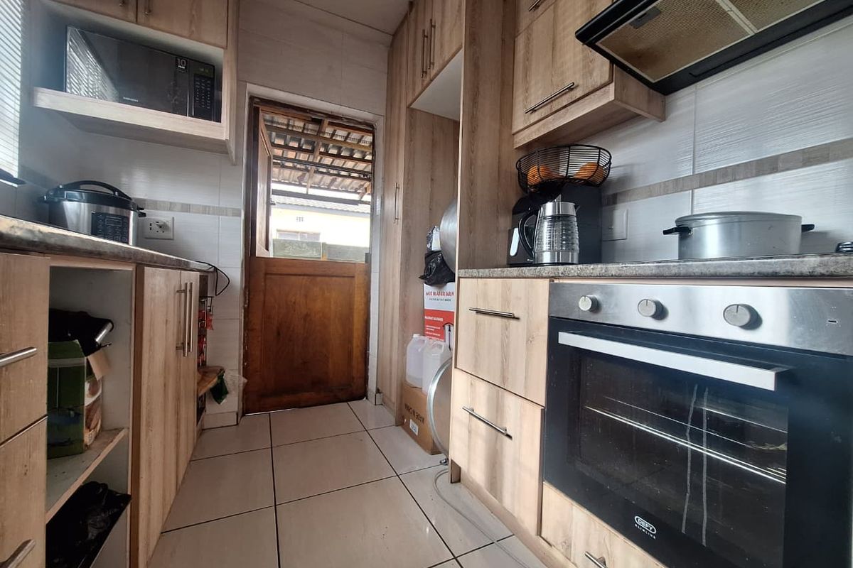A functional kitchen featuring light wood-finish cabinetry, built-in oven with extractor fan, tiled flooring, and direct access to the exterior via a stable door.