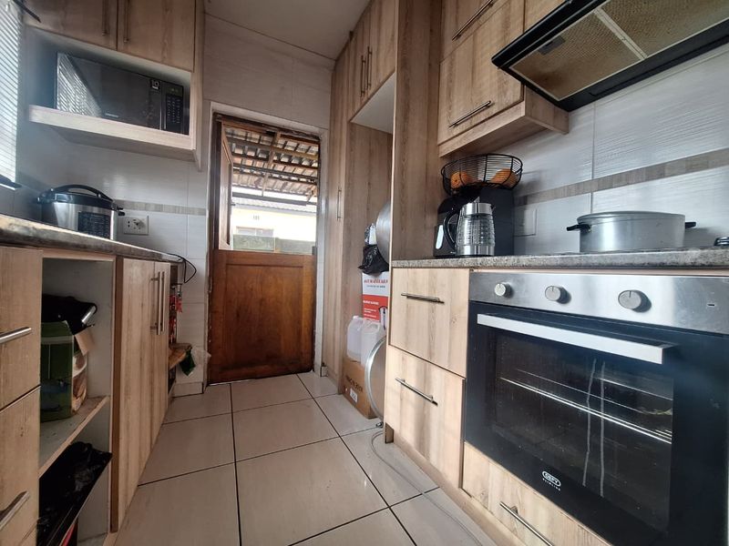 A functional kitchen featuring light wood-finish cabinetry, built-in oven with extractor fan, tiled flooring, and direct access to the exterior via a stable door.