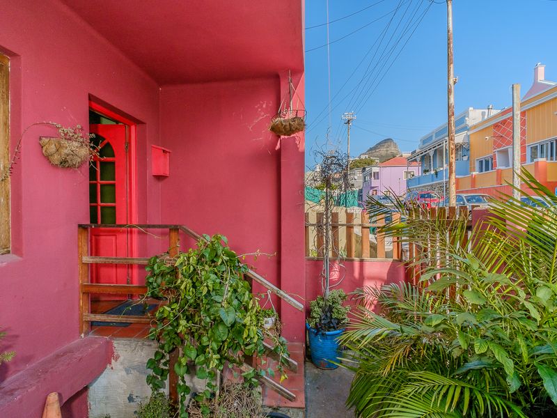 Front entrance area featuring a vibrant pink facade, timber handrail, and steps leading to a wooden front door.