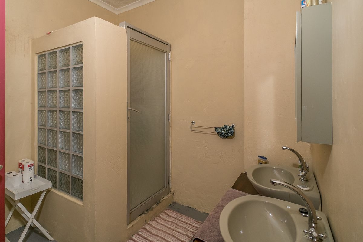 A functional bathroom featuring a double vanity with chrome taps and a shower enclosure with a glass block feature wall.