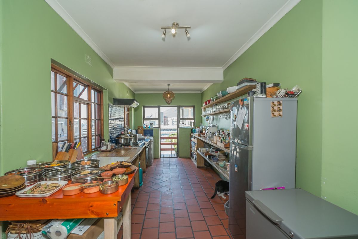 A galley-style kitchen featuring terracotta tile flooring, timber window frames, and open shelving, offering a functional layout with potential for modern updates.