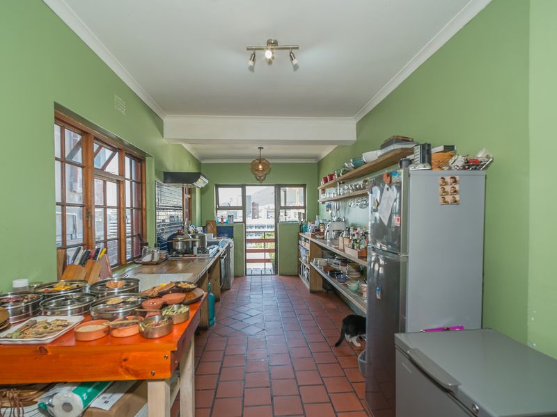 A galley-style kitchen featuring terracotta tile flooring, timber window frames, and open shelving, offering a functional layout with potential for modern updates.