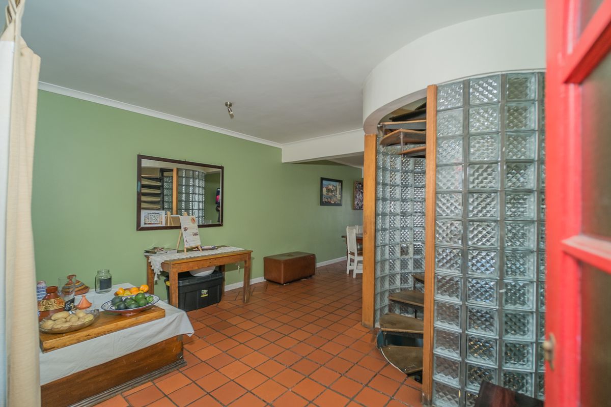 Living area featuring a distinctive spiral staircase enclosed by a glass block wall and traditional terracotta floor tiles.