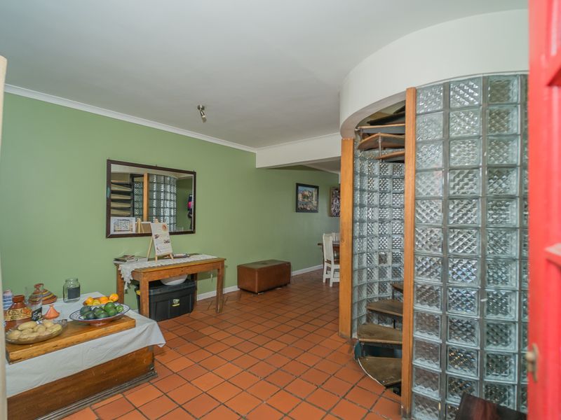 Living area featuring a distinctive spiral staircase enclosed by a glass block wall and traditional terracotta floor tiles.