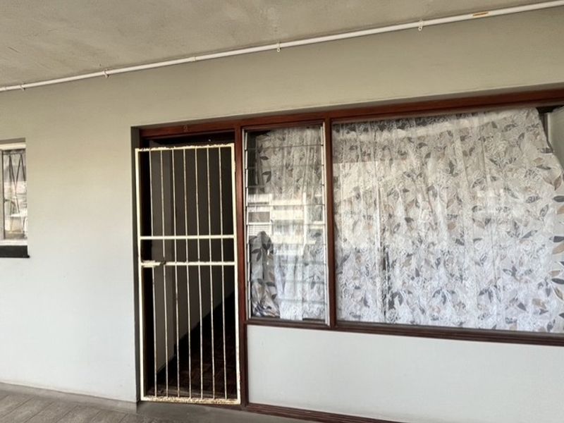 Apartment entrance featuring a security gate and timber-framed windows with exterior conduit visible along the wall.