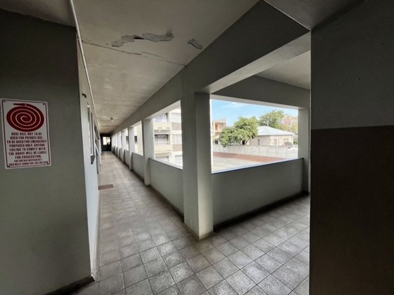 An open-air apartment complex hallway featuring tiled flooring and a concrete balustrade, showing signs of ceiling paint deterioration.