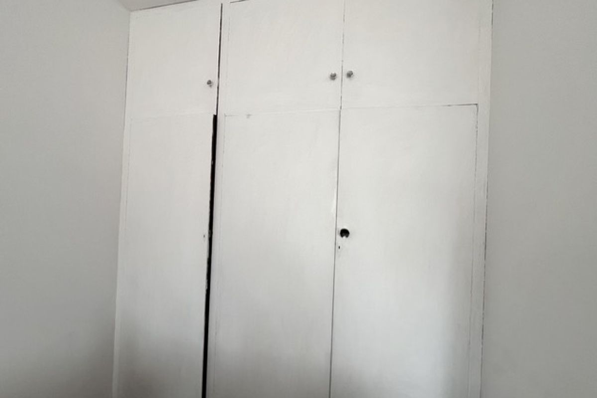 A bedroom featuring white built-in cupboards with overhead storage compartments, showing signs of wear and a missing handle.