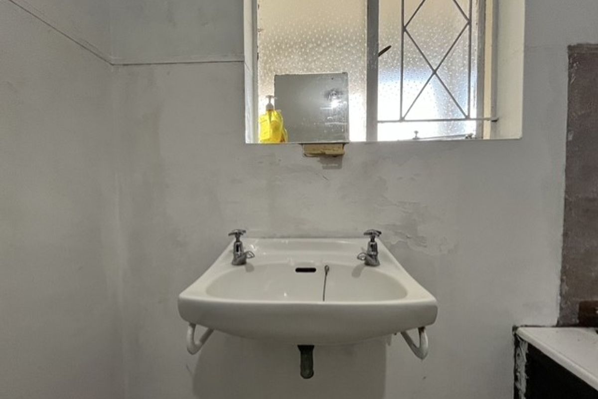A basic bathroom featuring a wall-mounted basin and an obscured glass window with security bars, currently requiring cosmetic wall repairs and updates.