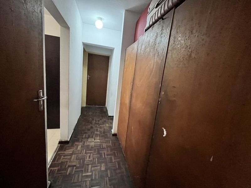 A narrow hallway featuring dark parquet flooring and built-in wooden cupboards, providing functional storage space within the apartment.