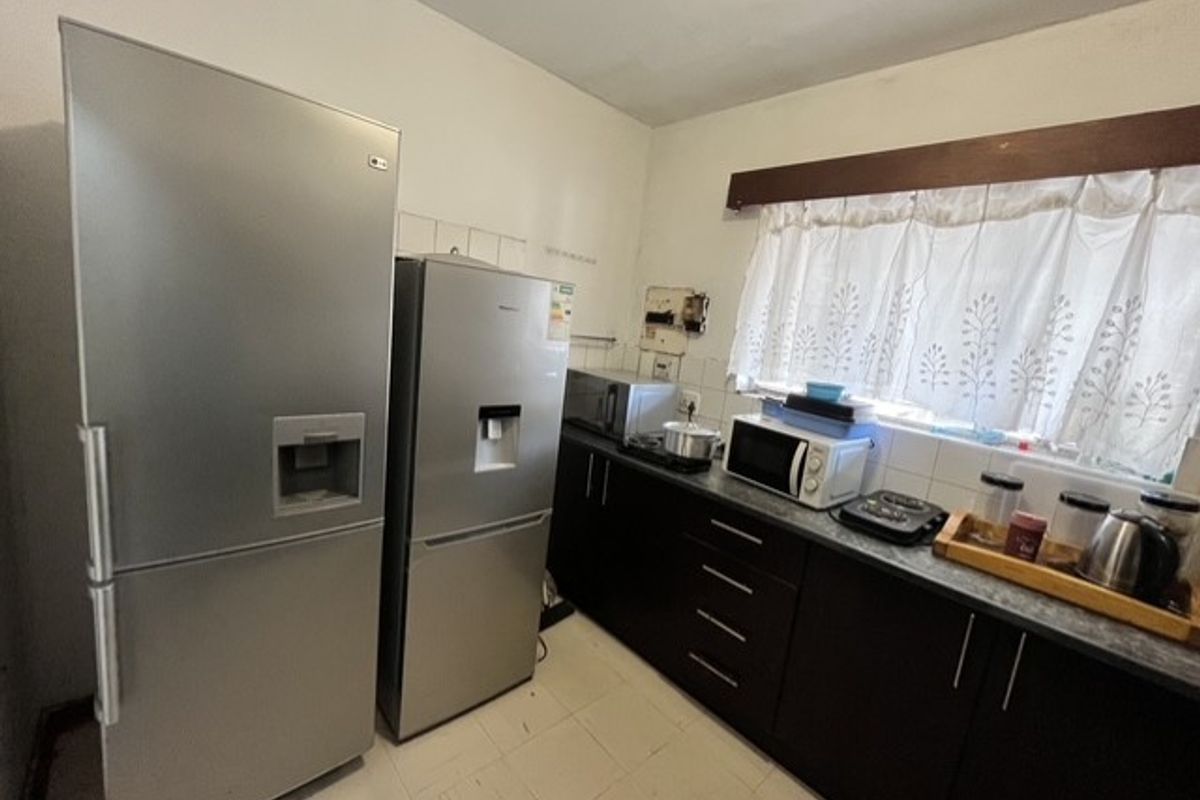 A functional kitchen featuring dark cabinetry, laminate countertops, and tiled flooring, offering a practical layout with ample space for appliances.