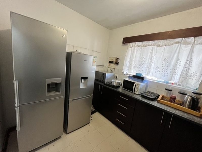 A functional kitchen featuring dark cabinetry, laminate countertops, and tiled flooring, offering a practical layout with ample space for appliances.