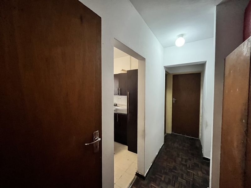 A functional hallway featuring parquet flooring and solid wood doors, providing access to adjacent rooms including a kitchen area.