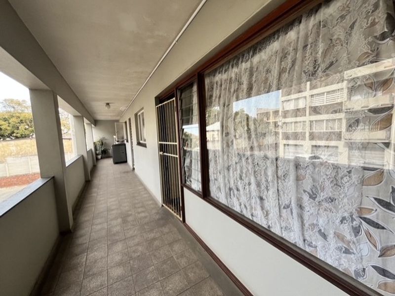 A covered balcony area featuring tiled flooring and a security gate, providing an outdoor walkway space for the apartment.