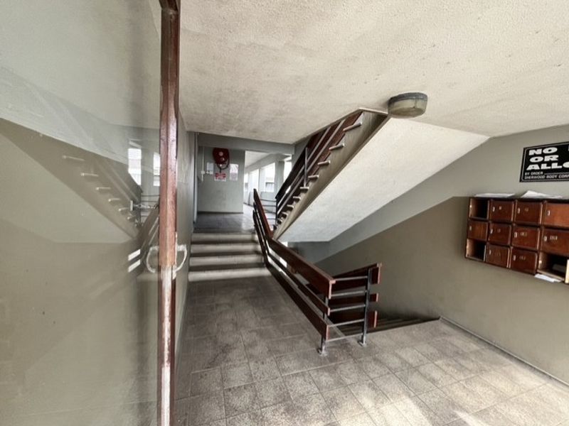 Communal apartment building hallway featuring a staircase with wooden handrails, tiled flooring, and built-in mailboxes.