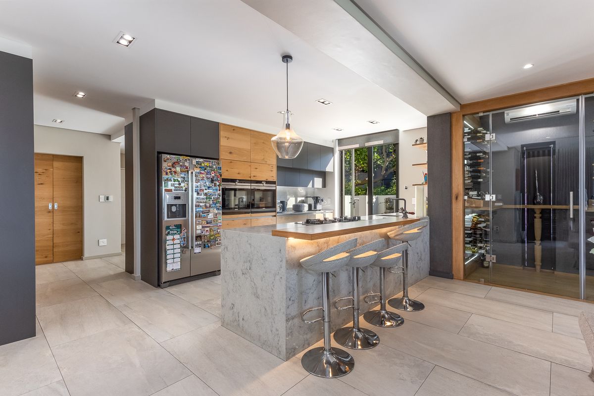 Modern open-plan kitchen featuring a stone island with breakfast bar, built-in appliances, sleek wooden cabinetry, and an integrated glass-enclosed wine cellar.