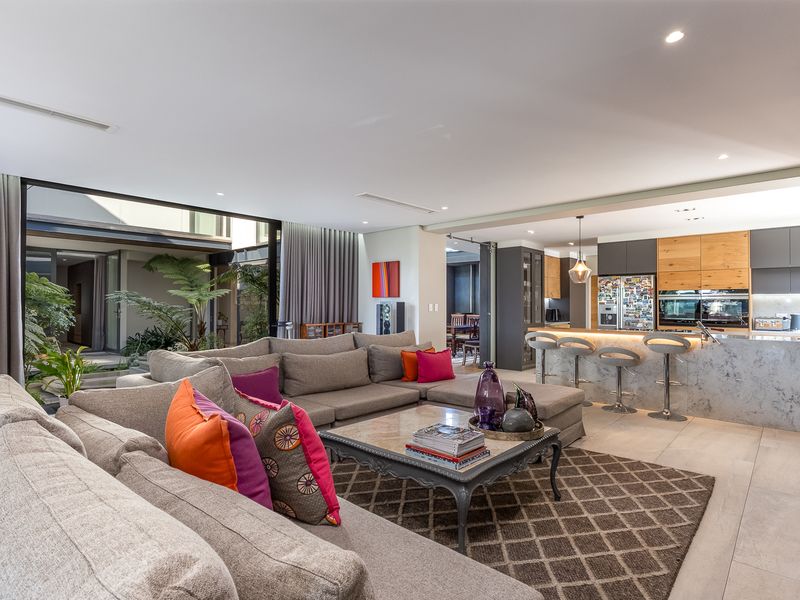 Spacious open-plan living area featuring a modern kitchen with stone island, integrated appliances, and seamless flow to an internal courtyard through large sliding doors.