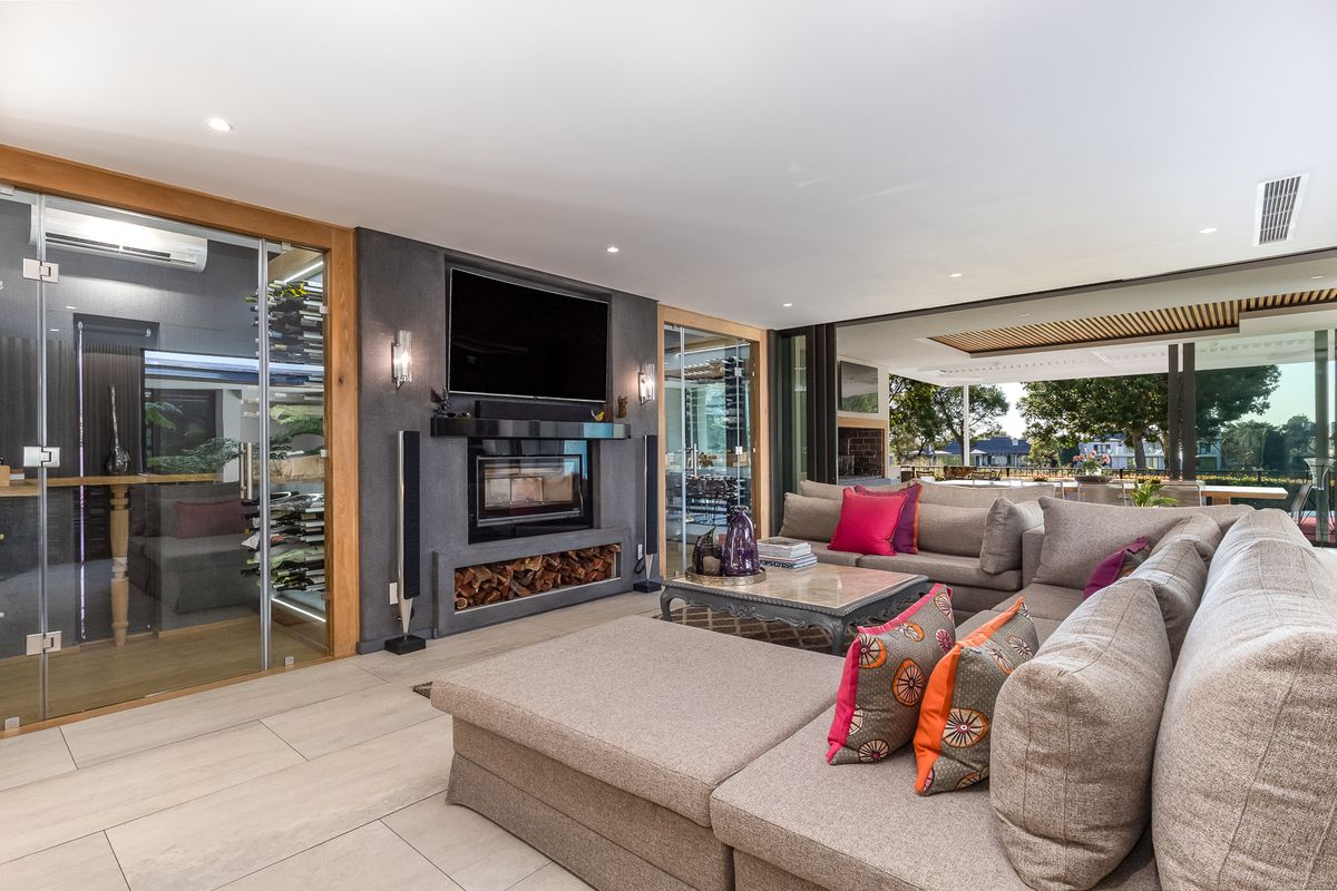 Modern living room featuring a built-in fireplace, integrated glass-enclosed wine cellar, and seamless flow to an outdoor patio through large sliding glass doors.