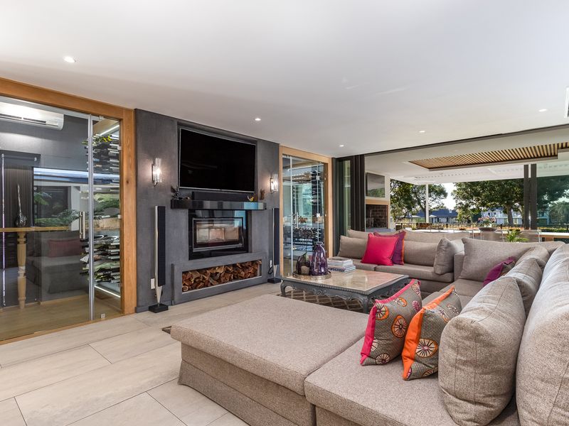 Modern living room featuring a built-in fireplace, integrated glass-enclosed wine cellar, and seamless flow to an outdoor patio through large sliding glass doors.