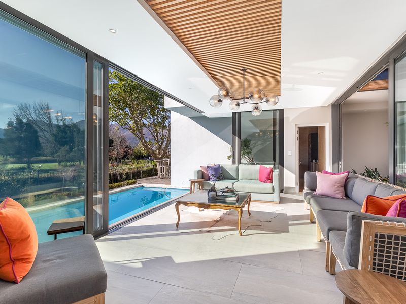 A modern covered patio featuring a slatted timber ceiling, large sliding glass doors, and seamless access to an adjacent swimming pool.