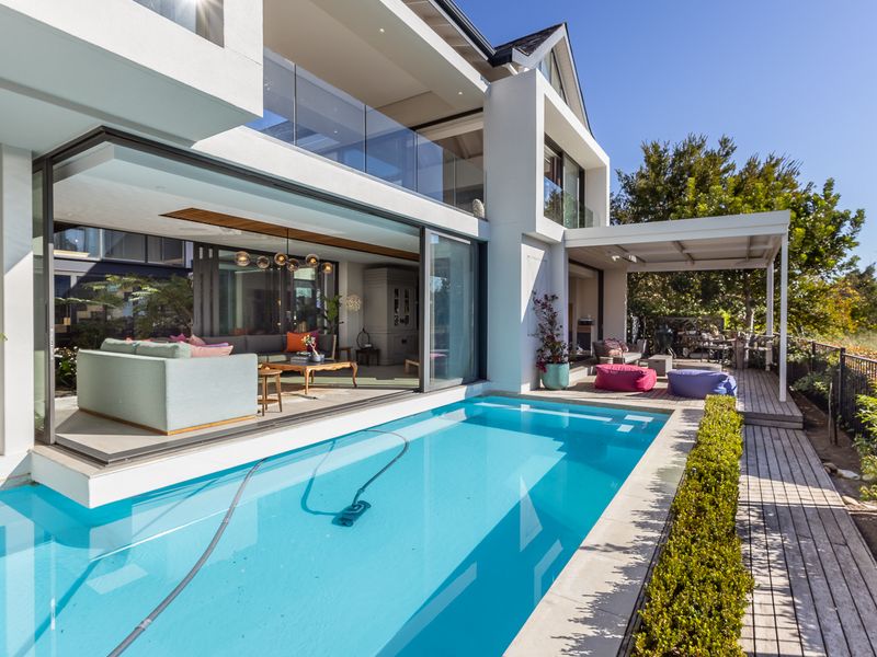 Modern luxury residence featuring a seamless indoor-outdoor flow with a swimming pool, timber decking, and expansive glass sliding doors opening to the living area.