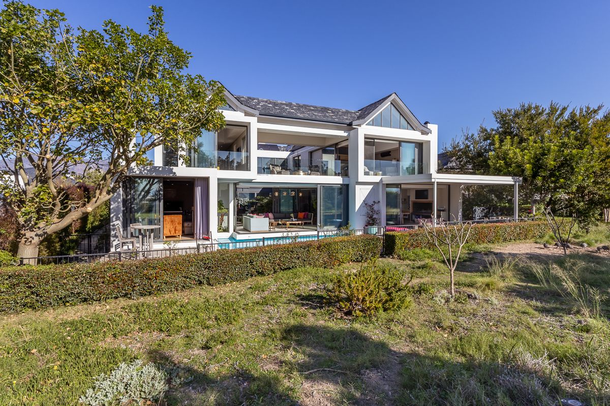 A modern two-story luxury residence featuring expansive sliding glass doors, a swimming pool, and a spacious covered patio overlooking the rear garden.