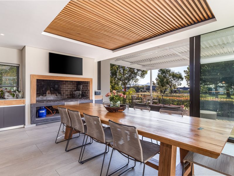 Modern covered patio featuring a built-in braai, timber slat ceiling detail, and large sliding glass doors opening to an outdoor garden area.