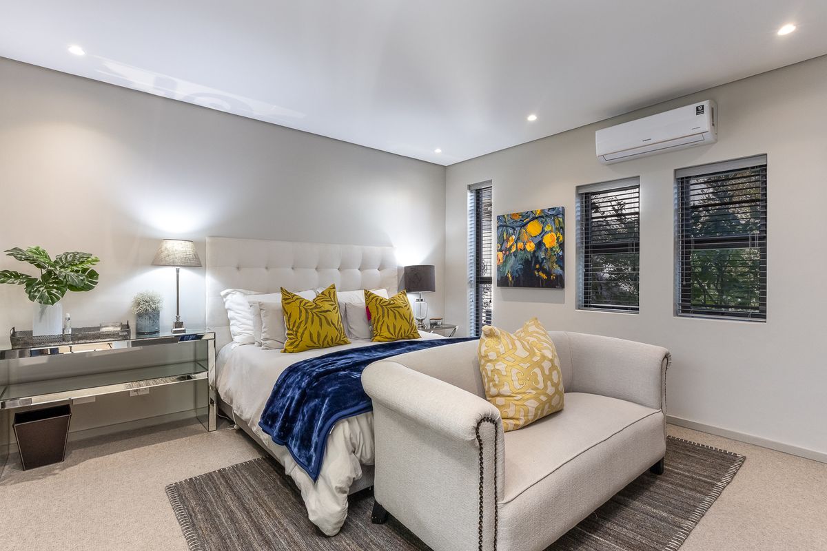 A well-maintained bedroom featuring neutral carpeting, recessed downlighting, and a wall-mounted split-system air conditioning unit.