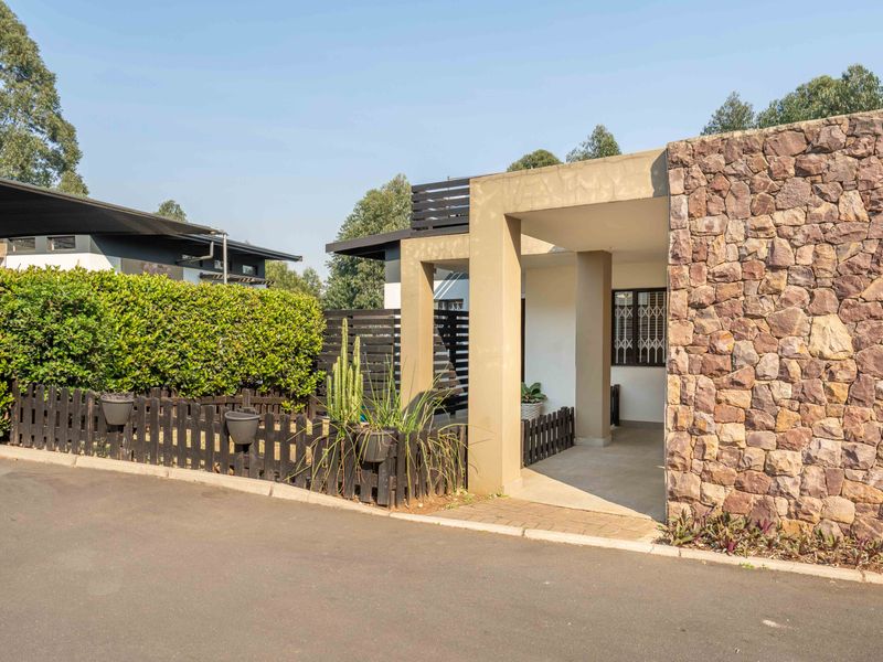Front elevation of the apartment featuring a stone-clad facade, concrete pillars, and a private entrance with security gate and timber fencing.