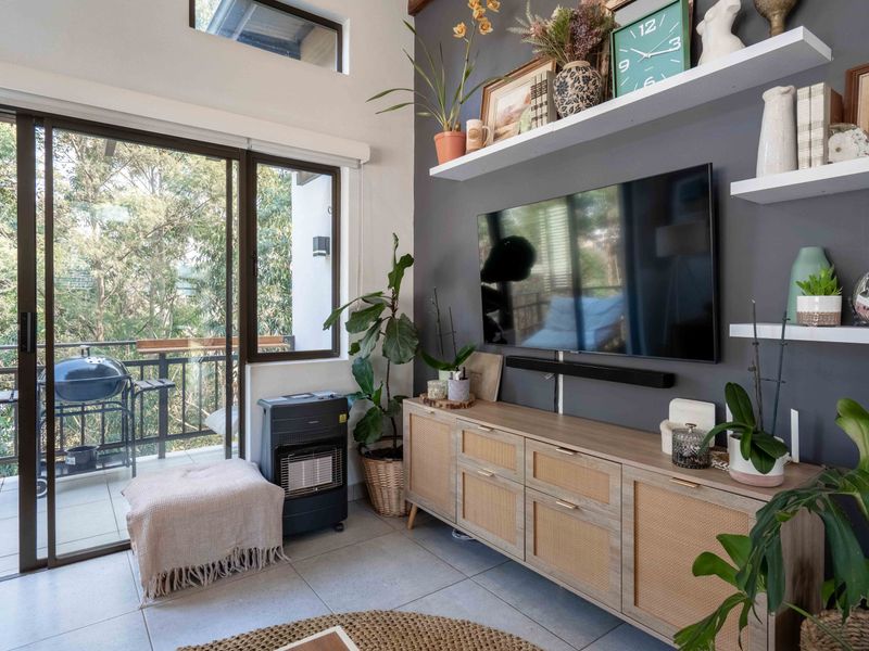 A bright living room featuring tiled floors, high ceilings with a clerestory window, and a sliding glass door leading to a balcony.