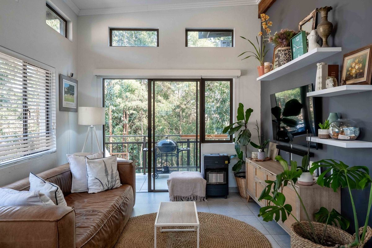 Bright living room featuring high ceilings with clerestory windows, tiled flooring, and direct access to a private balcony through sliding glass doors.