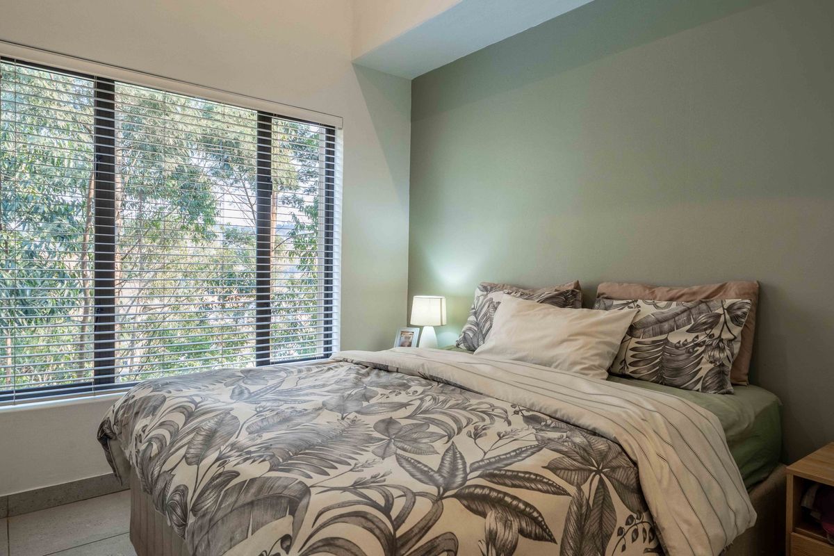 A well-lit bedroom featuring tiled flooring, large windows with venetian blinds, and a soft green accent wall.