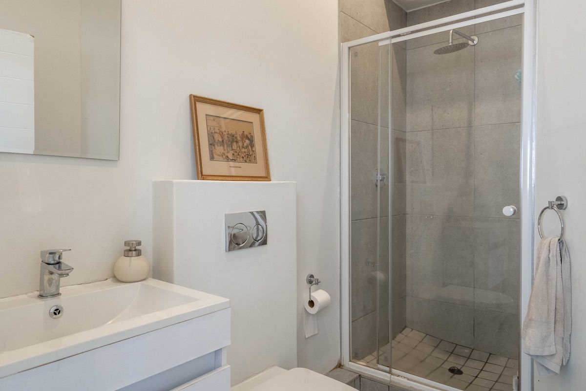Modern bathroom featuring a vanity basin, wall-mounted toilet with concealed cistern, and a glass-enclosed shower with grey tiling.