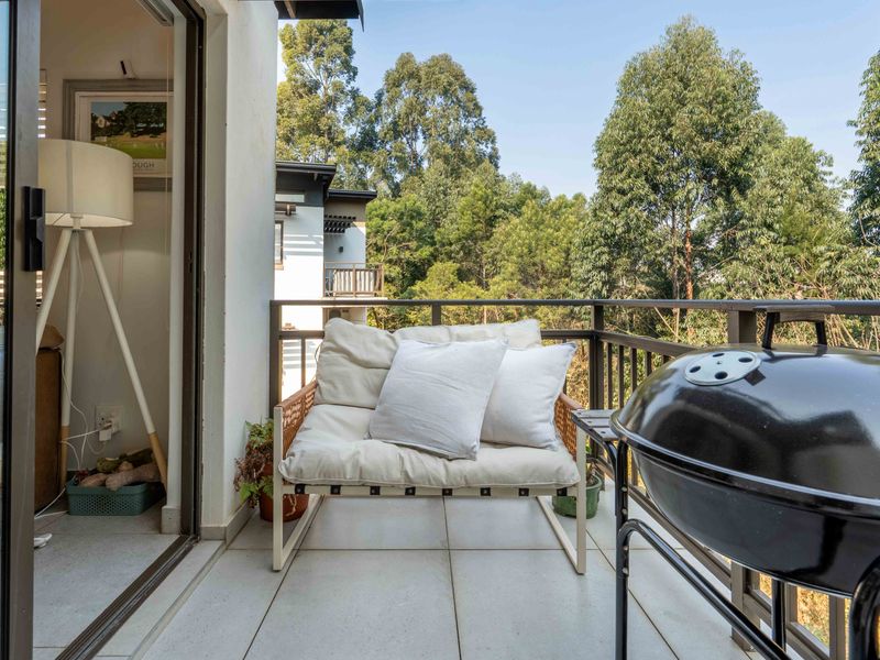 A private balcony featuring tiled flooring and a metal railing, offering a pleasant outdoor space with views of the surrounding trees.