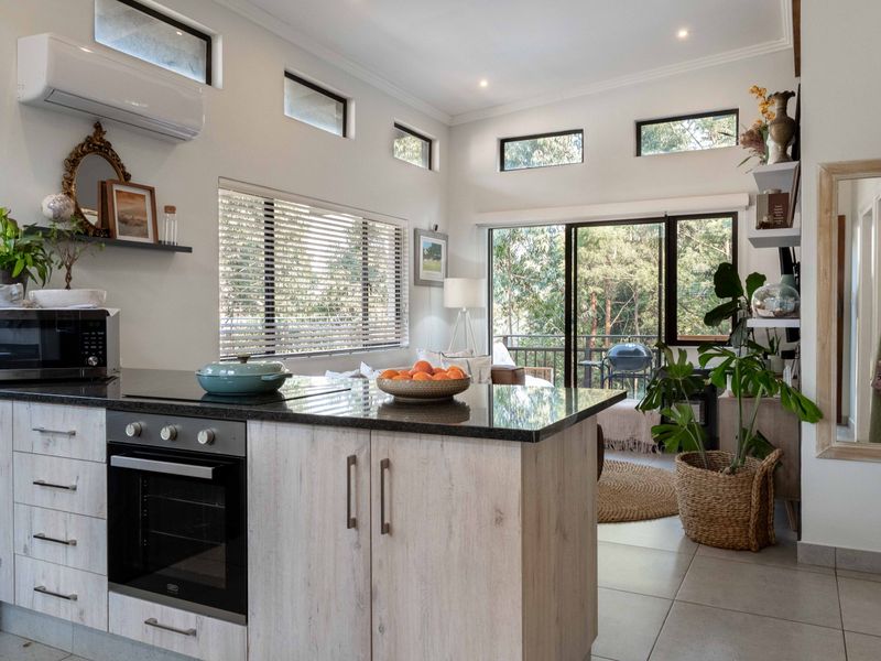 Modern open-plan kitchen and living area featuring a stone-topped island, built-in oven, split-system air conditioning, and large sliding doors leading to an outdoor balcony.