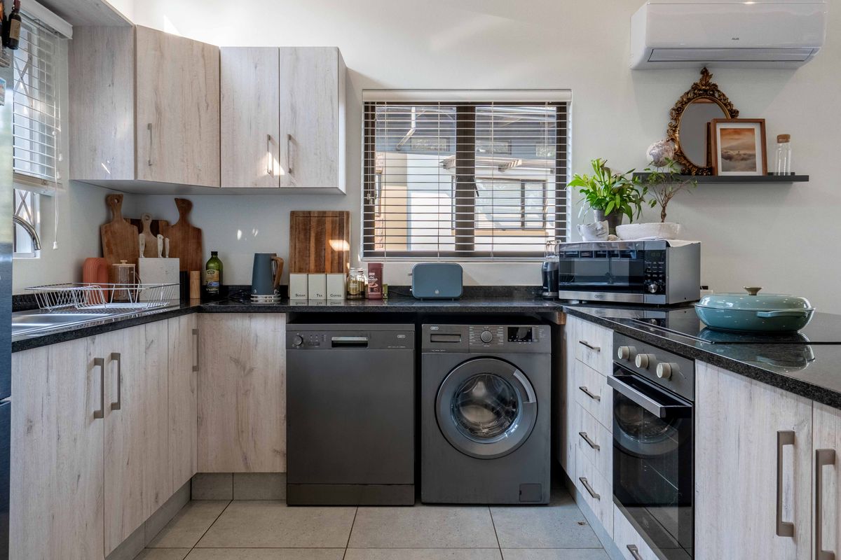 A well-maintained kitchen featuring light wood-grain cabinetry, dark granite countertops, integrated oven and hob, and tiled flooring with ample natural light.