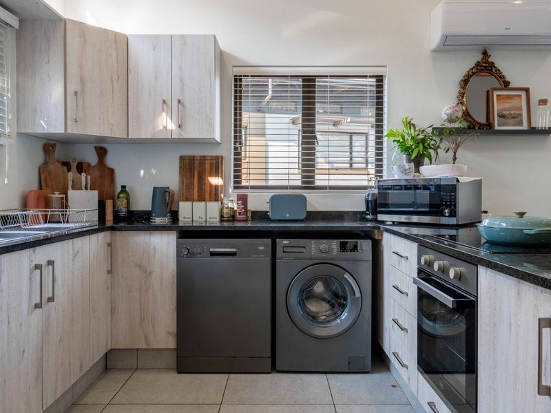 A well-maintained kitchen featuring light wood-grain cabinetry, dark granite countertops, integrated oven and hob, and tiled flooring with ample natural light.