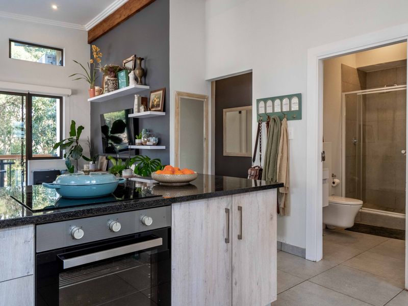 Modern open-plan kitchen featuring a granite island with built-in oven and hob, adjacent to a contemporary bathroom with a walk-in shower.