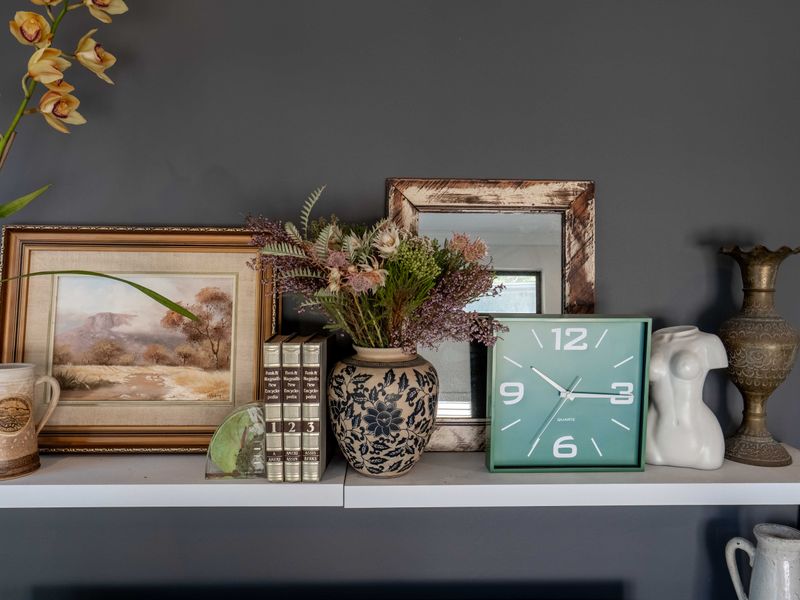 A close-up view of a decorative wall shelf featuring various personal ornaments and artwork against a dark grey painted wall.