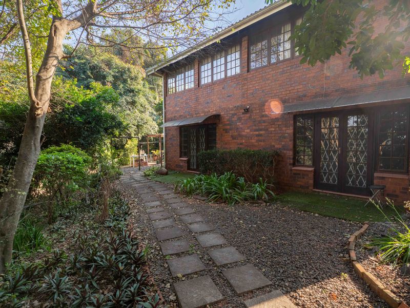 Rear view of a two-story brick house featuring a stone paver pathway, established garden landscaping, and secure metal-framed windows and doors.