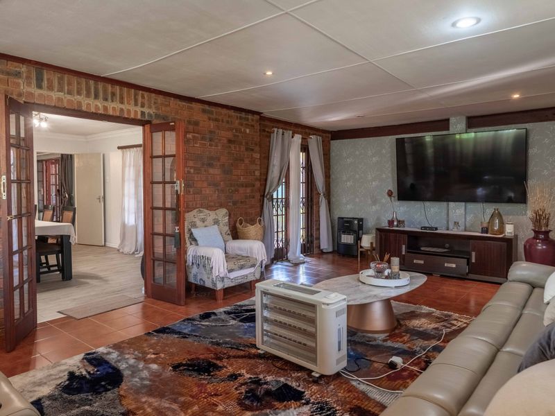 Spacious living room featuring exposed brick walls, tiled flooring, and french doors leading to the exterior, creating a warm and inviting atmosphere.